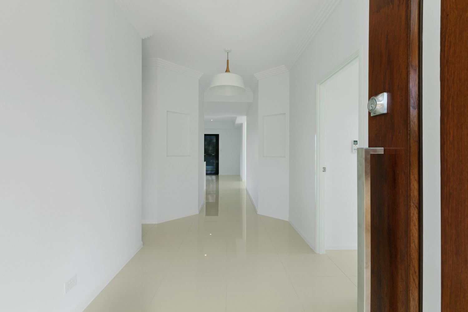 An Empty Hallway With White Walls and a Wooden Door — Ashlee Jones Homes in Gordonvale, QLD