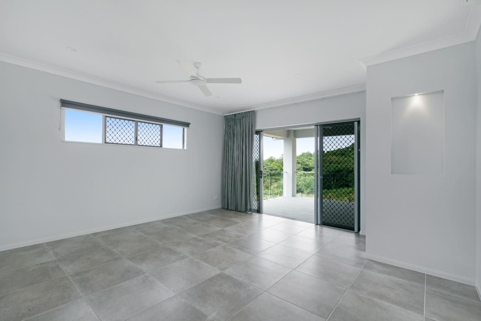 An Empty Living Room With a Ceiling Fan and Sliding Glass Doors — Ashlee Jones Homes in Gordonvale, QLD