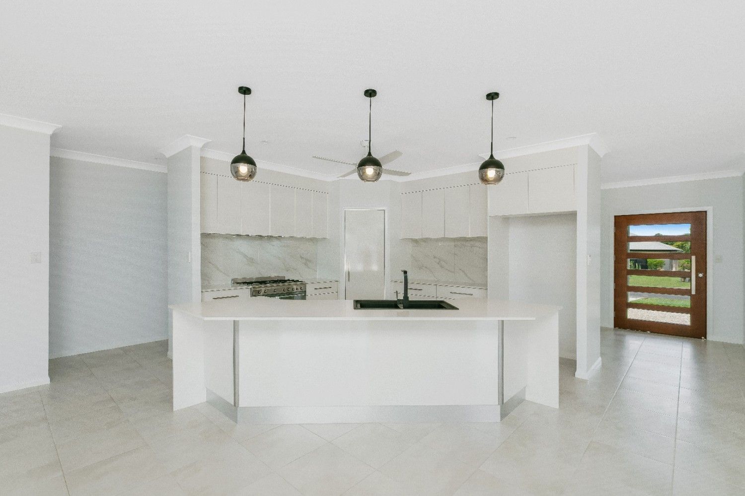 An Empty Kitchen With White Cabinets and a Large Island — Ashlee Jones Homes in Gordonvale, QLD