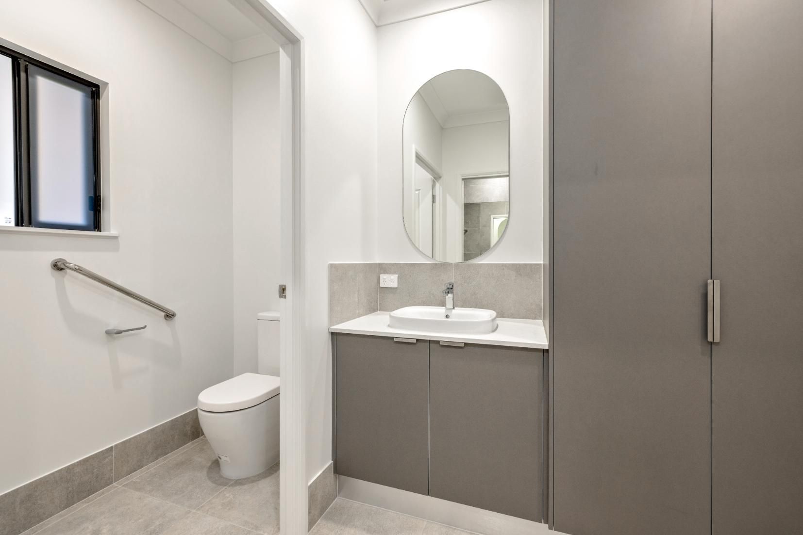 A Bathroom With a Toilet, Sink and Mirror — Ashlee Jones Homes in Gordonvale, QLD