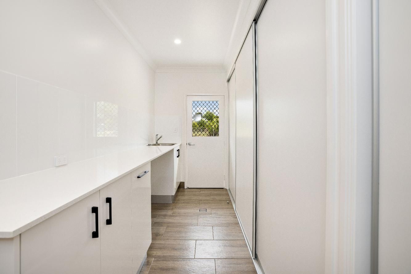 A Long Hallway With White Cabinets and Sliding Glass Doors Leading to a Kitchen — Ashlee Jones Homes in Gordonvale, QLD