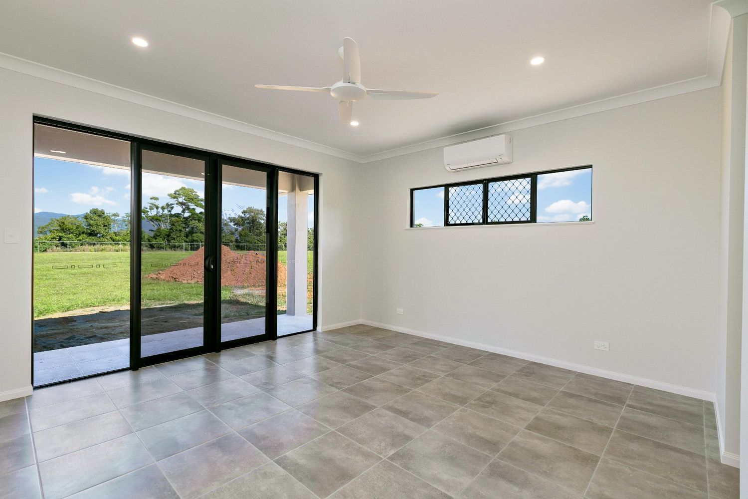 An Empty Living Room With Sliding Glass Doors and a Ceiling Fan — Ashlee Jones Homes in Gordonvale, QLD