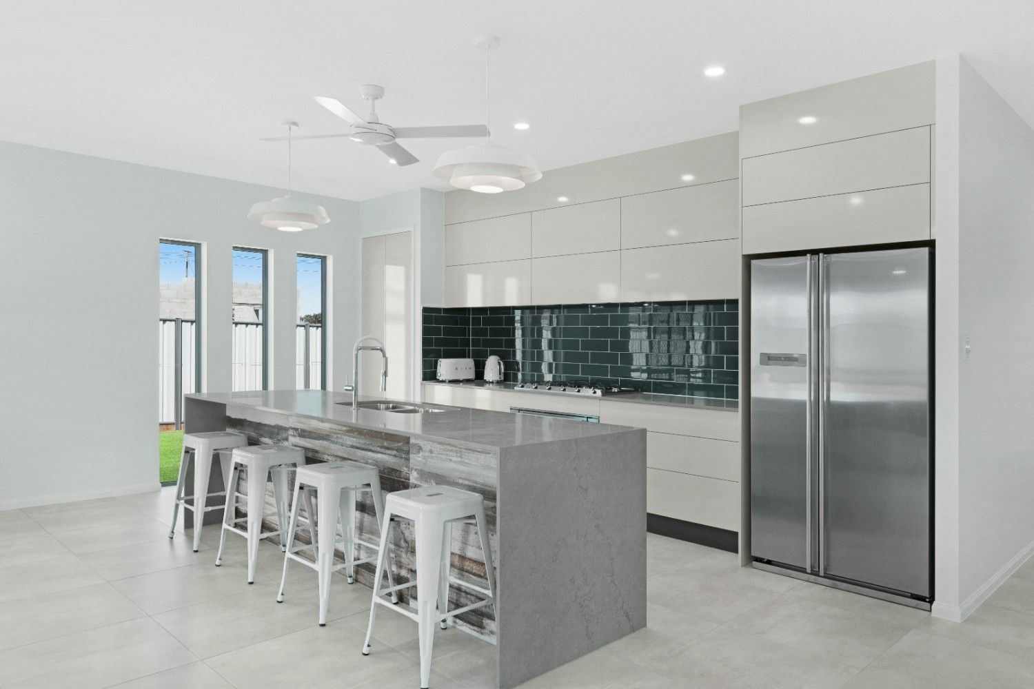 A Kitchen With a Large Island, Stools, a Refrigerator and a Ceiling Fan — Ashlee Jones Homes in Gordonvale, QLD