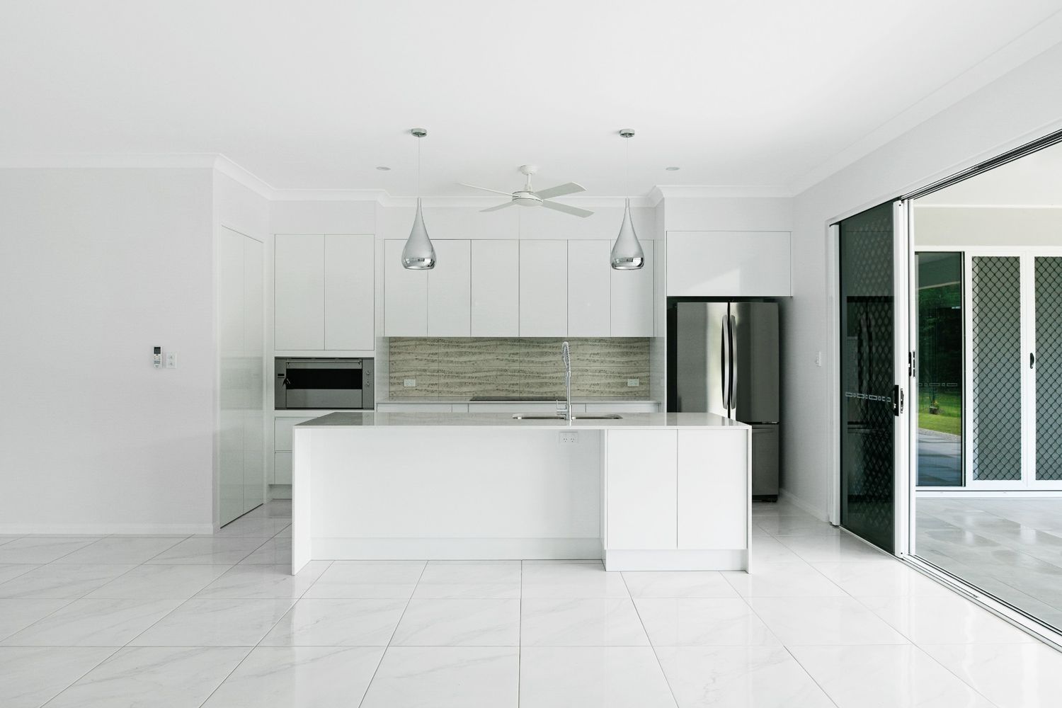 An Empty Kitchen With White Cabinets and Stainless Steel Appliances — Ashlee Jones Homes in Gordonvale, QLD