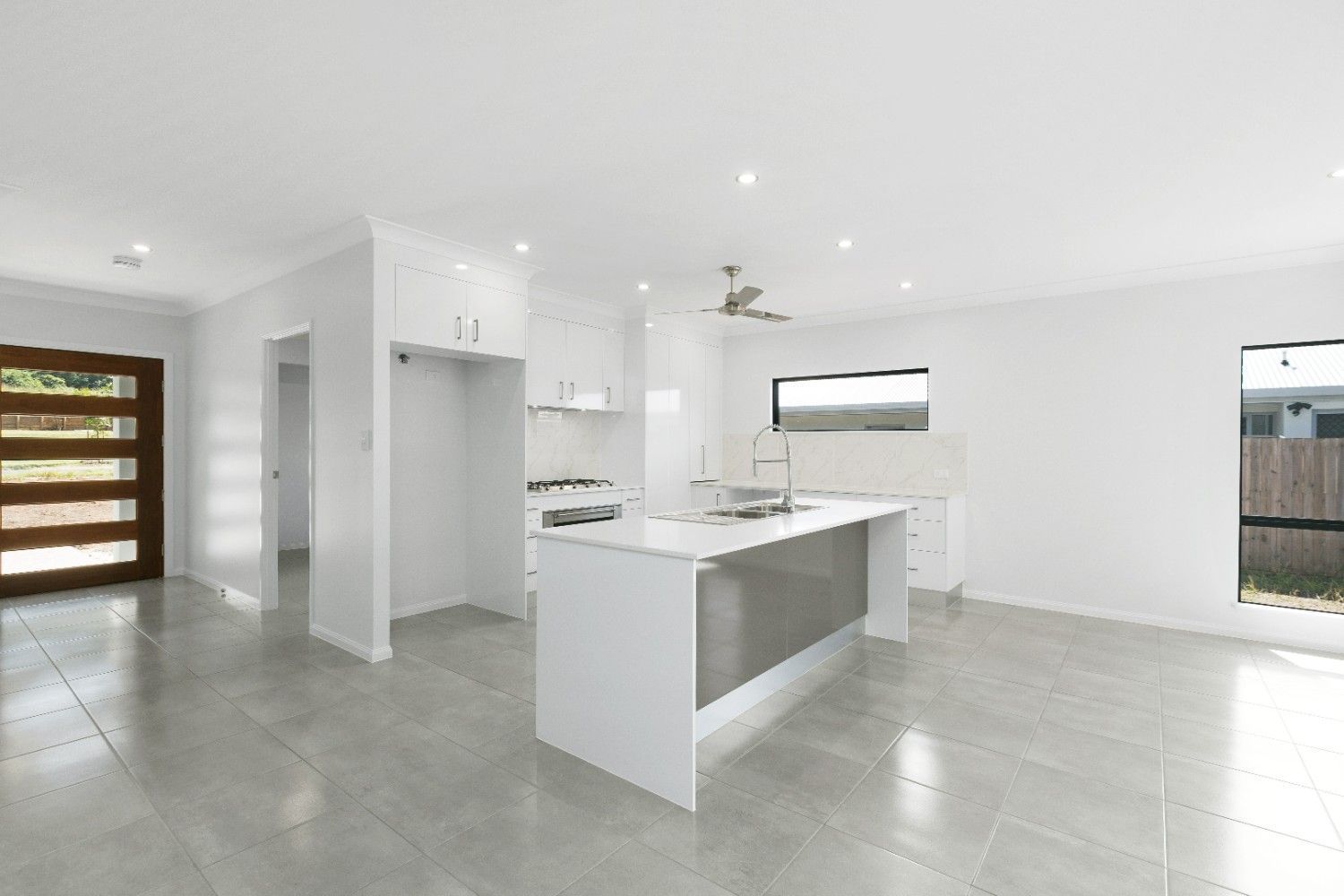 An Empty Kitchen in a House With White Cabinets and a Large Island — Ashlee Jones Homes in Gordonvale, QLD