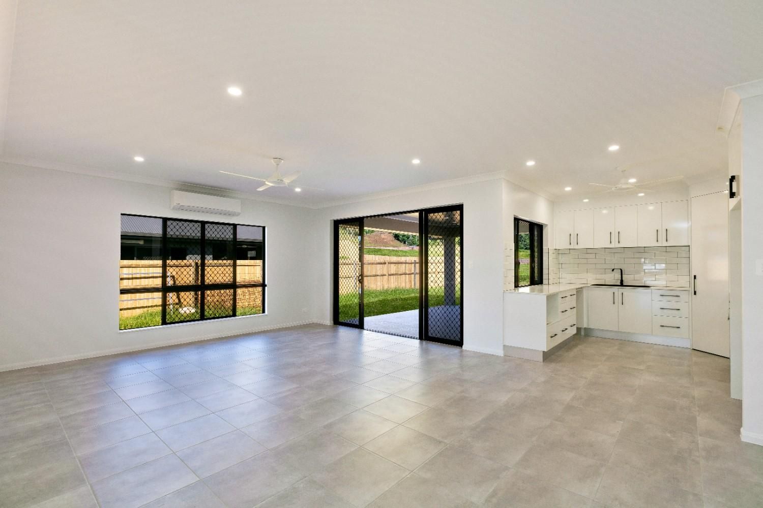 An Empty Living Room With a Kitchen and Sliding Glass Doors  — Ashlee Jones Homes in Gordonvale, QLD