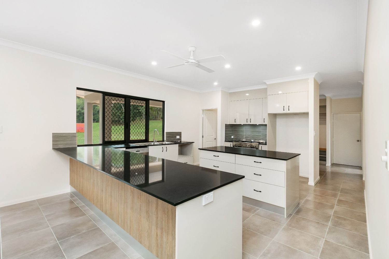 A Kitchen With White Cabinets, Black Counter Tops, and a Ceiling Fan — Ashlee Jones Homes in Gordonvale, QLD