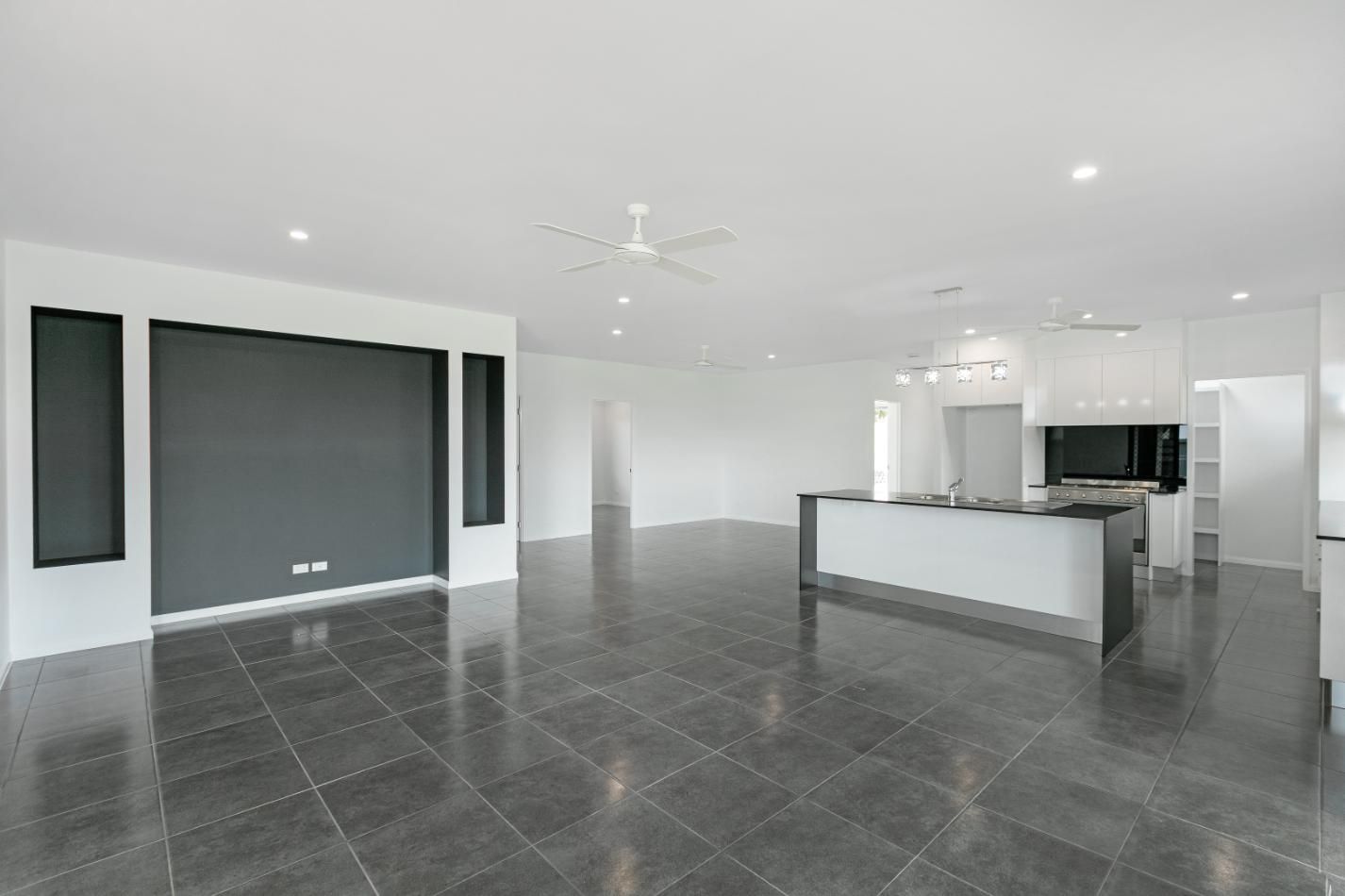 A Large Empty Room With a Black Tile Floor and a Ceiling Fan — Ashlee Jones Homes in Gordonvale, QLD