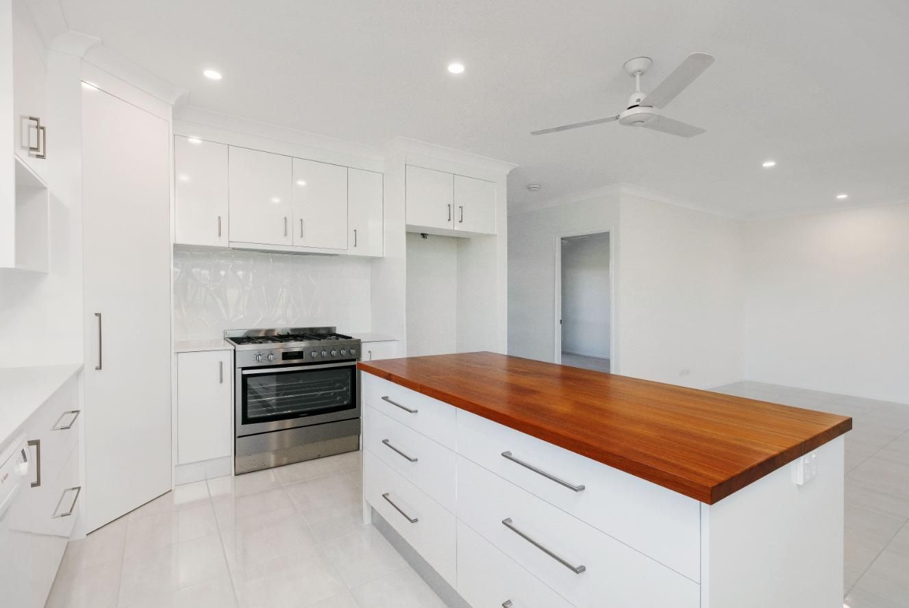 A Kitchen With White Cabinets and a Large Wooden Island — Ashlee Jones Homes in Gordonvale, QLD