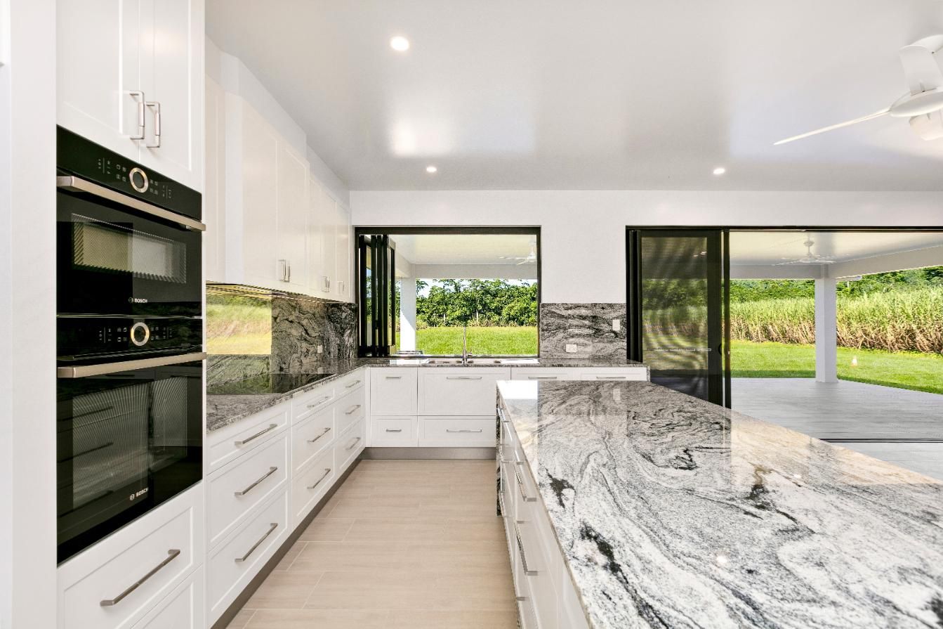 A Kitchen With Granite Counter Tops and White Cabinets — Ashlee Jones Homes in Gordonvale, QLD