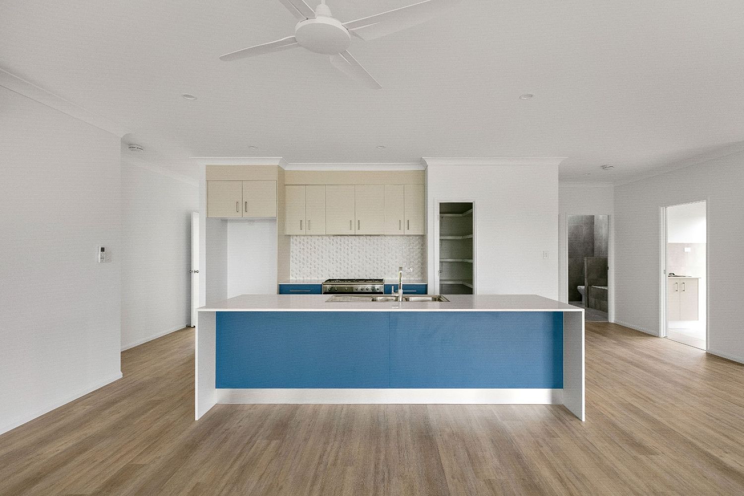 An Empty Kitchen With a Blue Island and a Ceiling Fan — Ashlee Jones Homes in Gordonvale, QLD