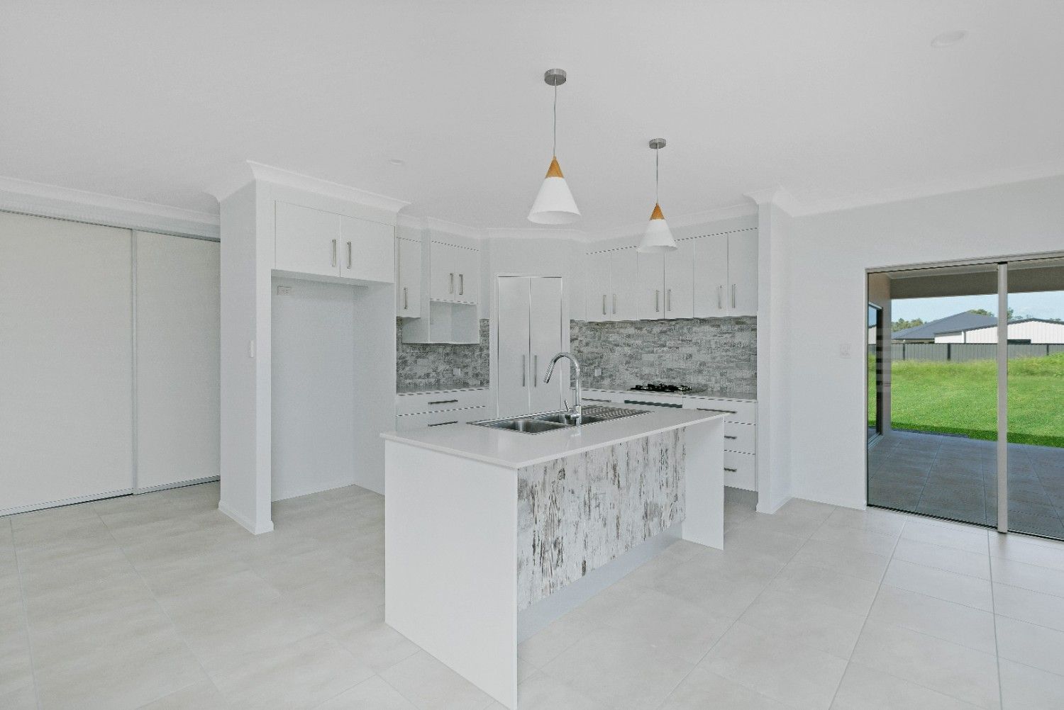 An Empty Kitchen With White Cabinets and a Large Island — Ashlee Jones Homes in Gordonvale, QLD
