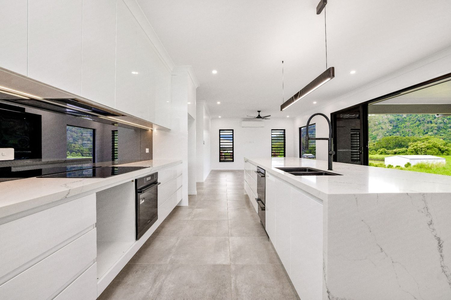 A Kitchen With White Cabinets and Black Appliances and a Large Island — Ashlee Jones Homes in Gordonvale, QLD