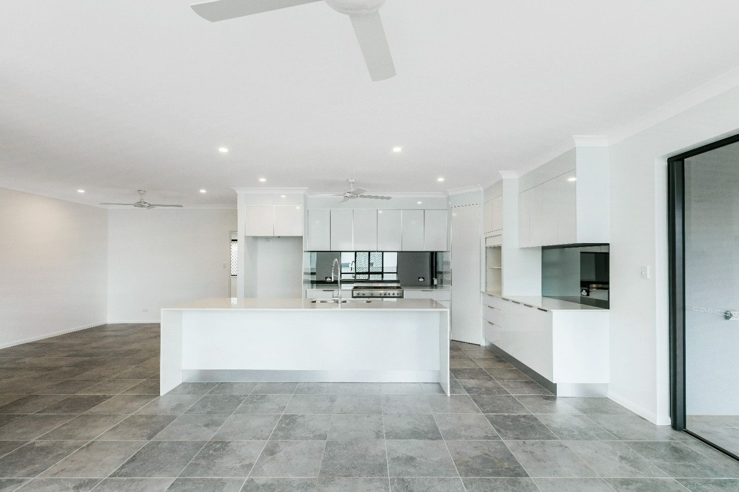 An Empty Kitchen With White Cabinets and a Ceiling Fan — Ashlee Jones Homes in Gordonvale, QLD