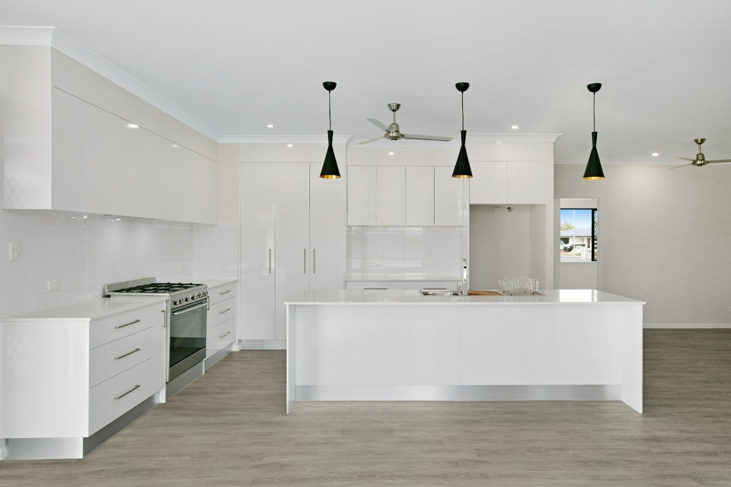 An Empty Kitchen With White Cabinets and a Large Island — Ashlee Jones Homes in Gordonvale, QLD