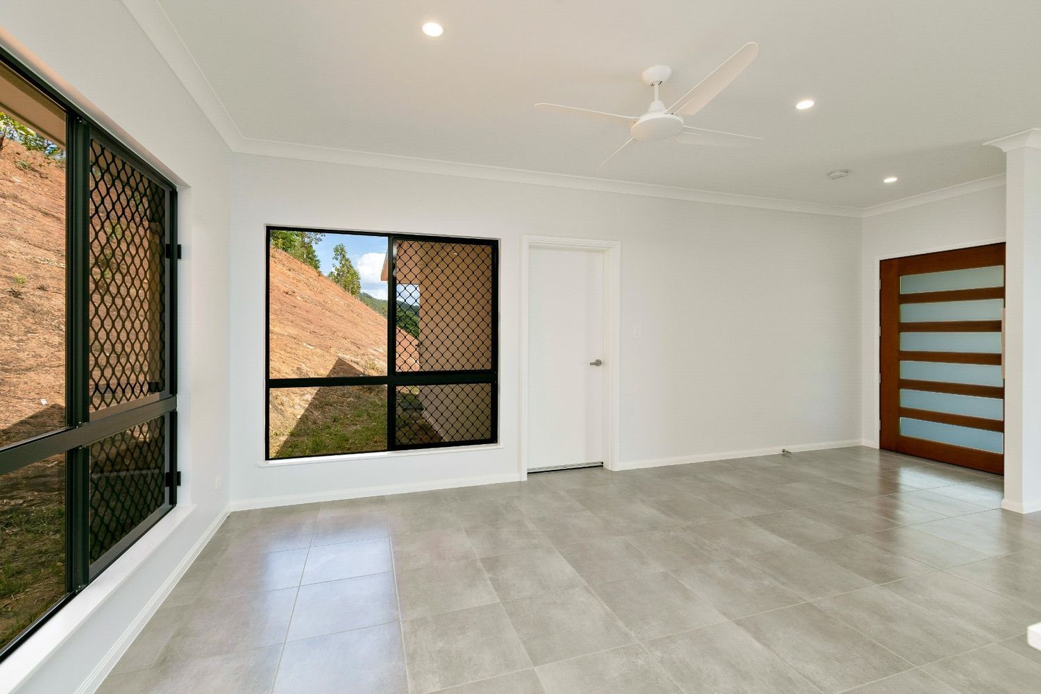 An Empty Living Room With a Ceiling Fan and Two Windows — Ashlee Jones Homes in Gordonvale, QLD