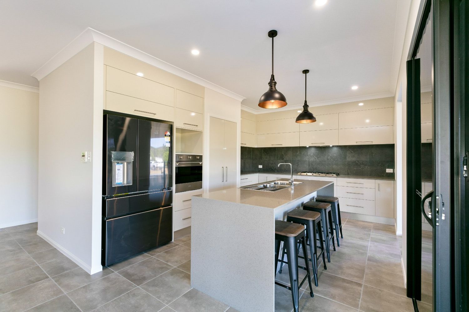 A Kitchen With a Large Island and Stools and a Black Refrigerator — Ashlee Jones Homes in Gordonvale, QLD