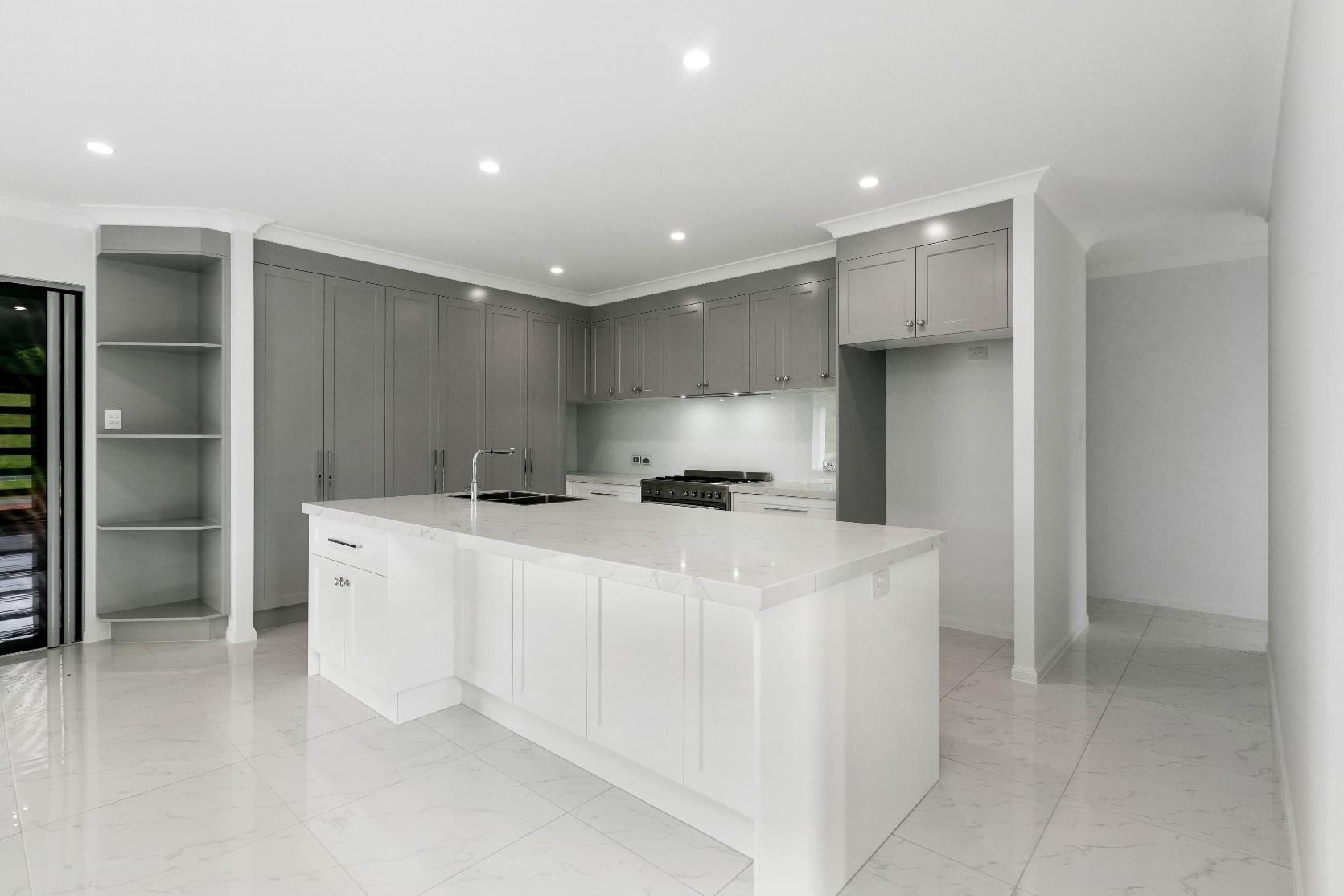An Empty Kitchen With White Cabinets and a Large Island — Ashlee Jones Homes in Gordonvale, QLD