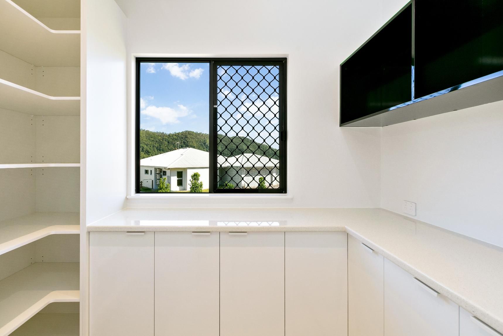 A Kitchen With White Cabinets and a Window With a View of a House — Ashlee Jones Homes in Gordonvale, QLD