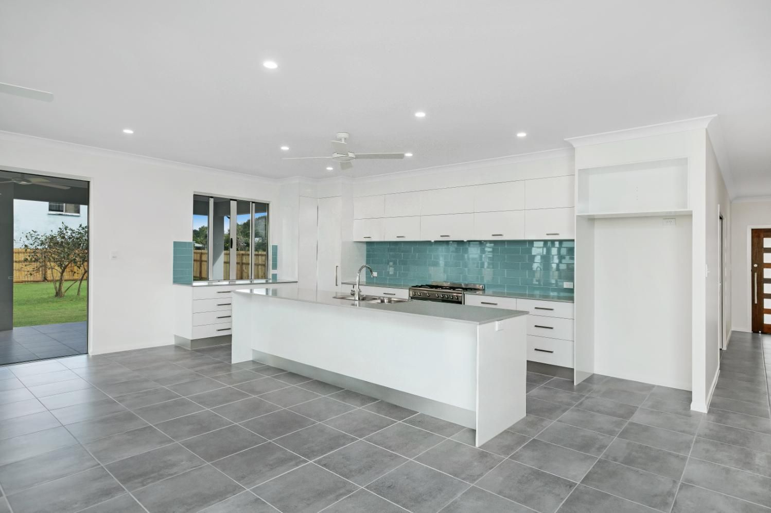 An Empty Kitchen With White Cabinets and a Large Island — Ashlee Jones Homes in Gordonvale, QLD