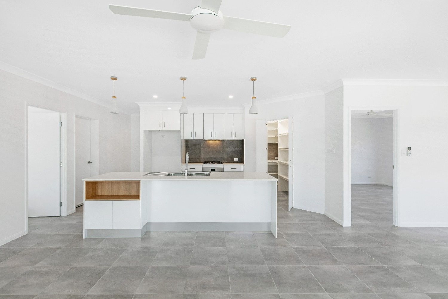 An Empty Kitchen With White Cabinets and a Ceiling Fan — Ashlee Jones Homes in Gordonvale, QLD