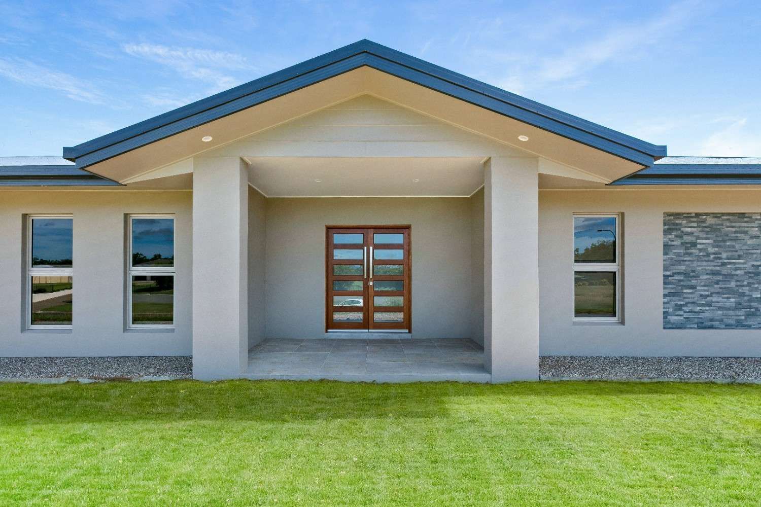 A White House With a Blue Roof and a Wooden Door is Sitting on Top of a Lush Green Lawn — Ashlee Jones Homes in Gordonvale, QLD