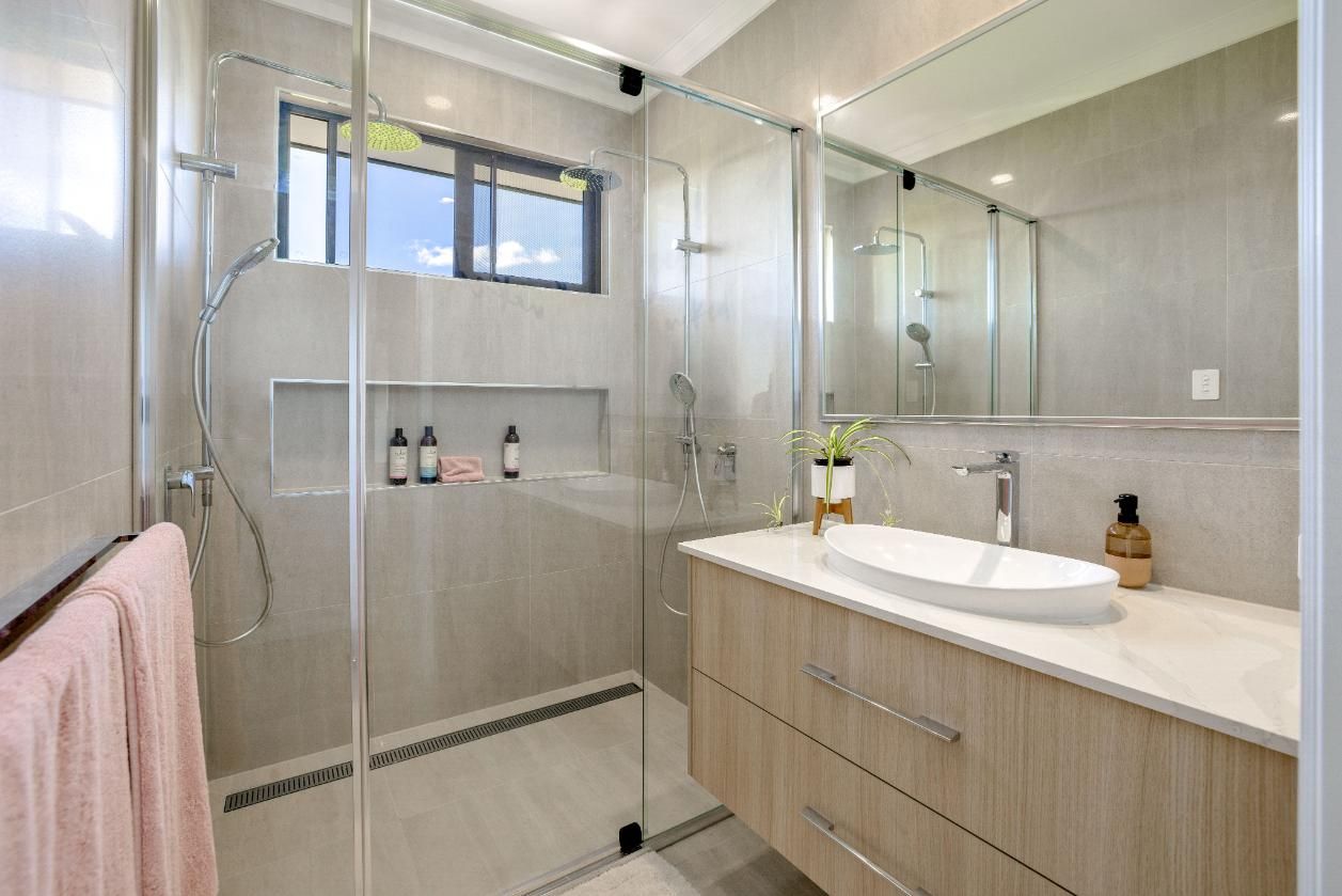 A Bathroom With a Sink, Mirror and Walk in Shower — Ashlee Jones Homes in Gordonvale, QLD