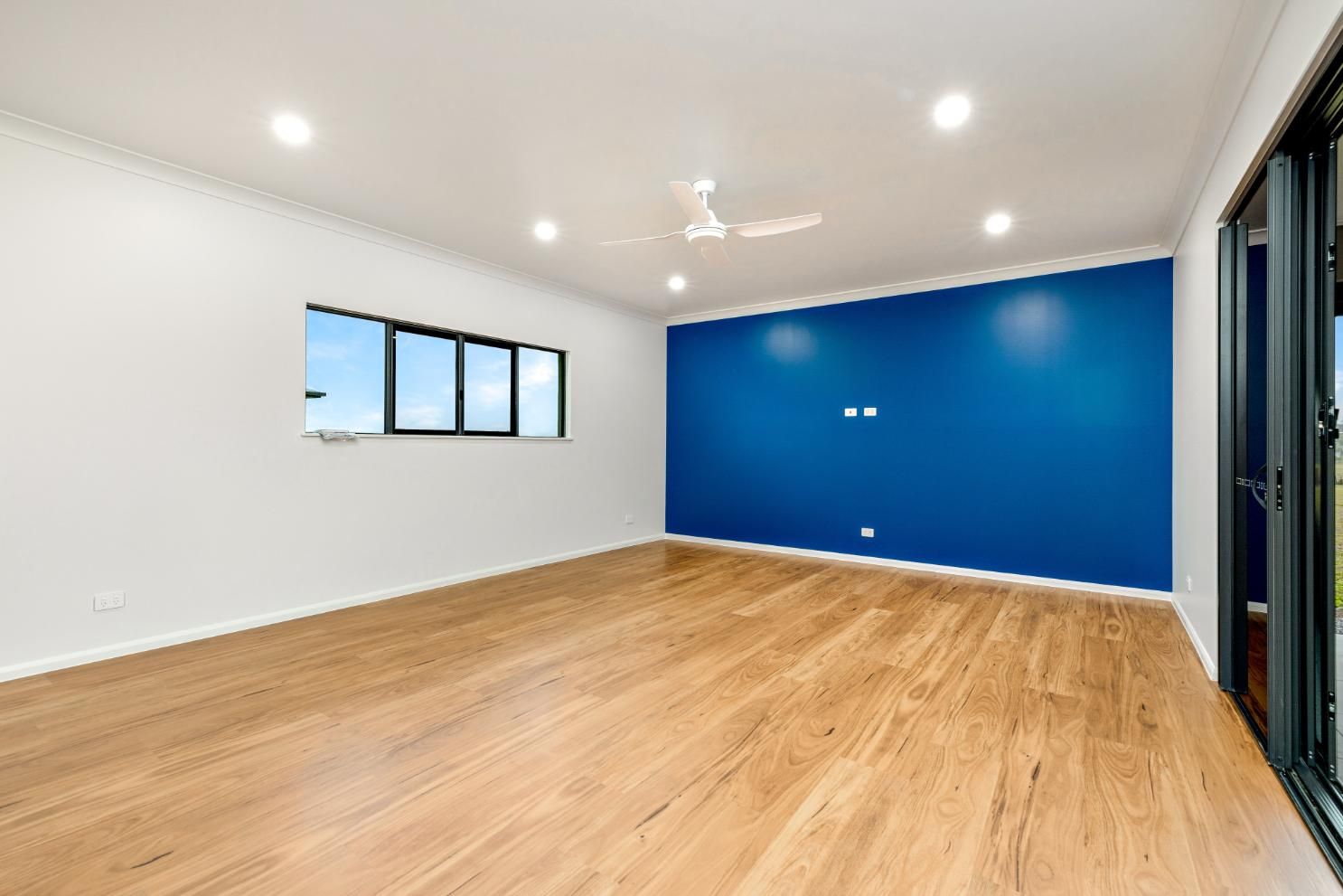 An Empty Living Room With a Blue Wall and Wooden Floor — Ashlee Jones Homes in Gordonvale, QLD