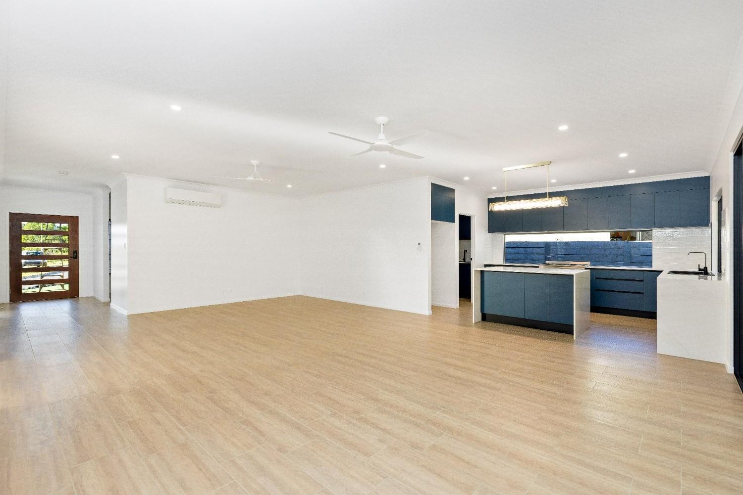 A Large Empty Room With Hardwood Floors and a Kitchen in the Background — Ashlee Jones Homes in Gordonvale, QLD
