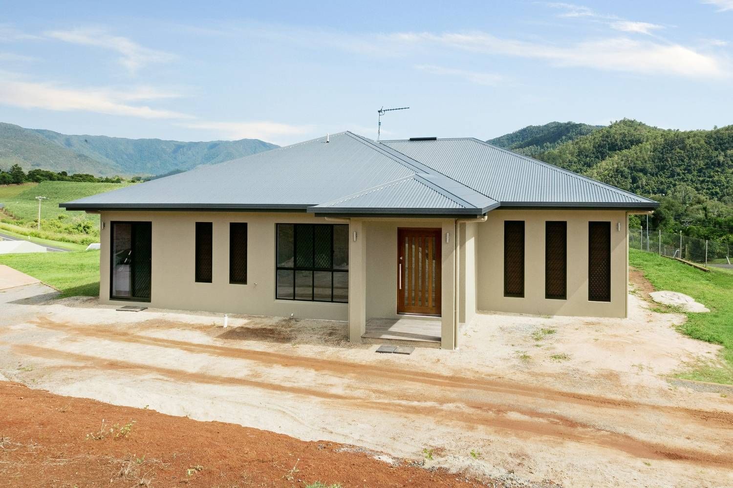A House is Sitting on Top of a Dirt Hill With Mountains in the Background — Ashlee Jones Homes in Gordonvale, QLD