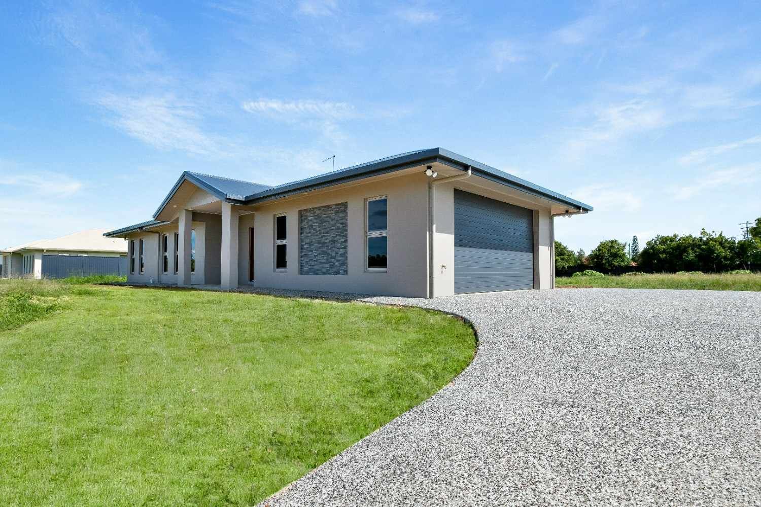 A House is Sitting on Top of a Lush Green Field Next to a Gravel Driveway — Ashlee Jones Homes in Gordonvale, QLD