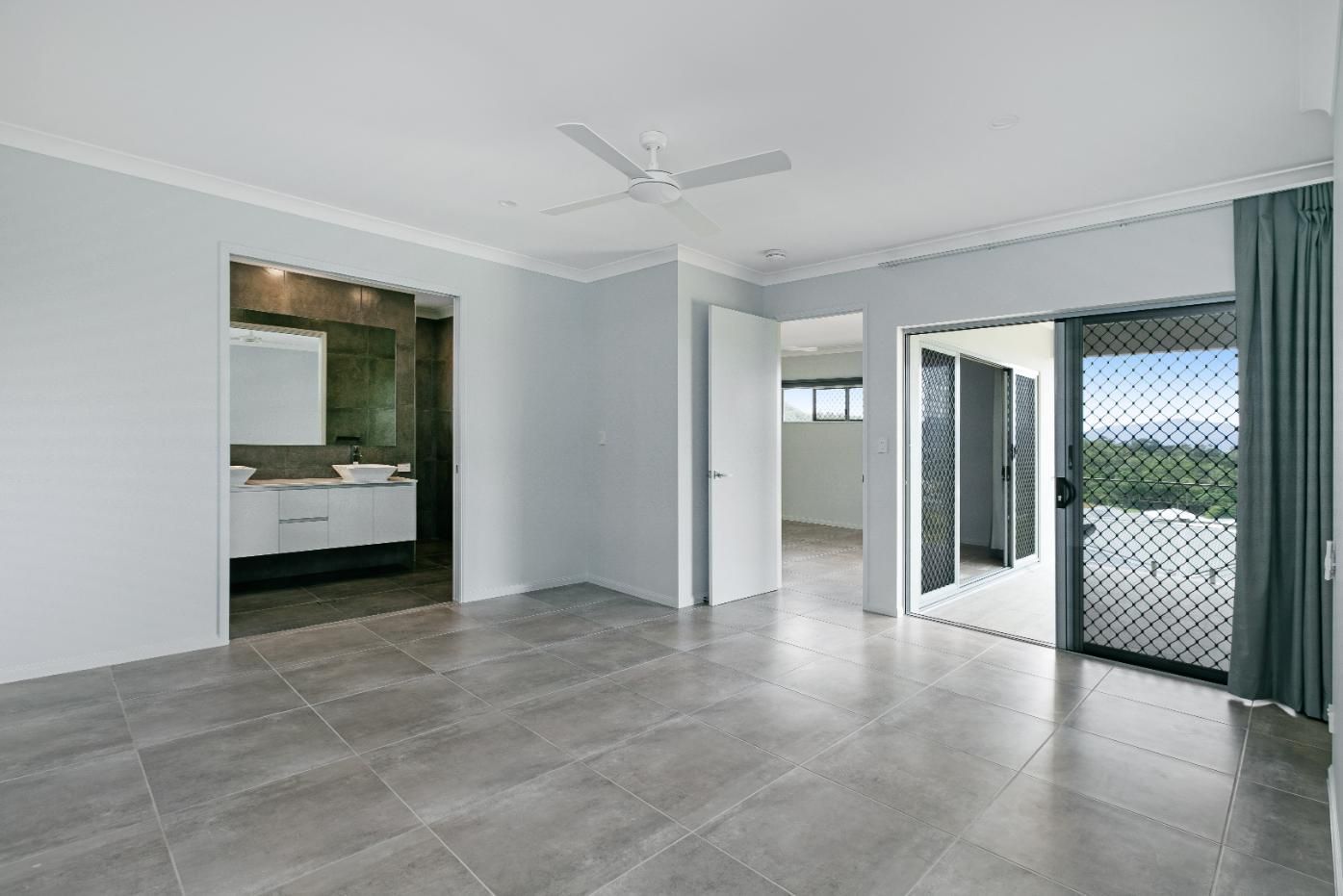A Large Empty Room With a Ceiling Fan and Sliding Glass Doors Leading to a Bathroom — Ashlee Jones Homes in Gordonvale, QLD