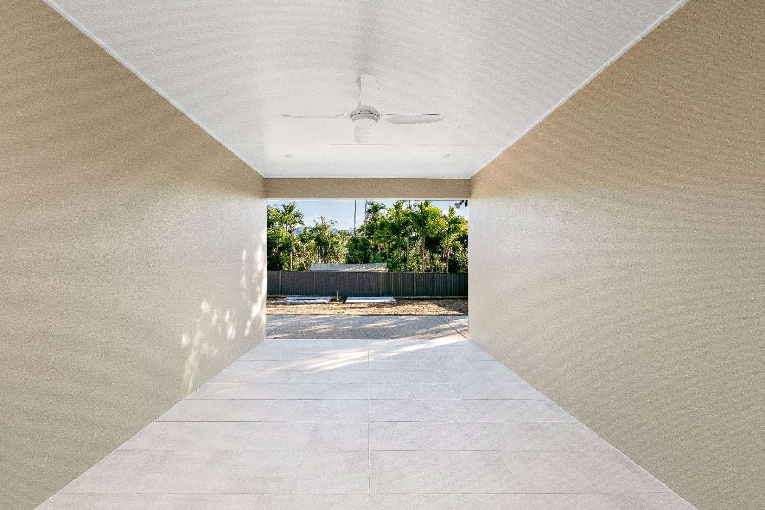 An Empty Garage With a Ceiling Fan and a View of the Backyard — Ashlee Jones Homes in Gordonvale, QLD