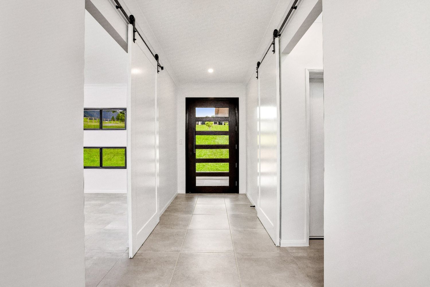 A Long Hallway With Sliding Barn Doors and a Black Door — Ashlee Jones Homes in Gordonvale, QLD