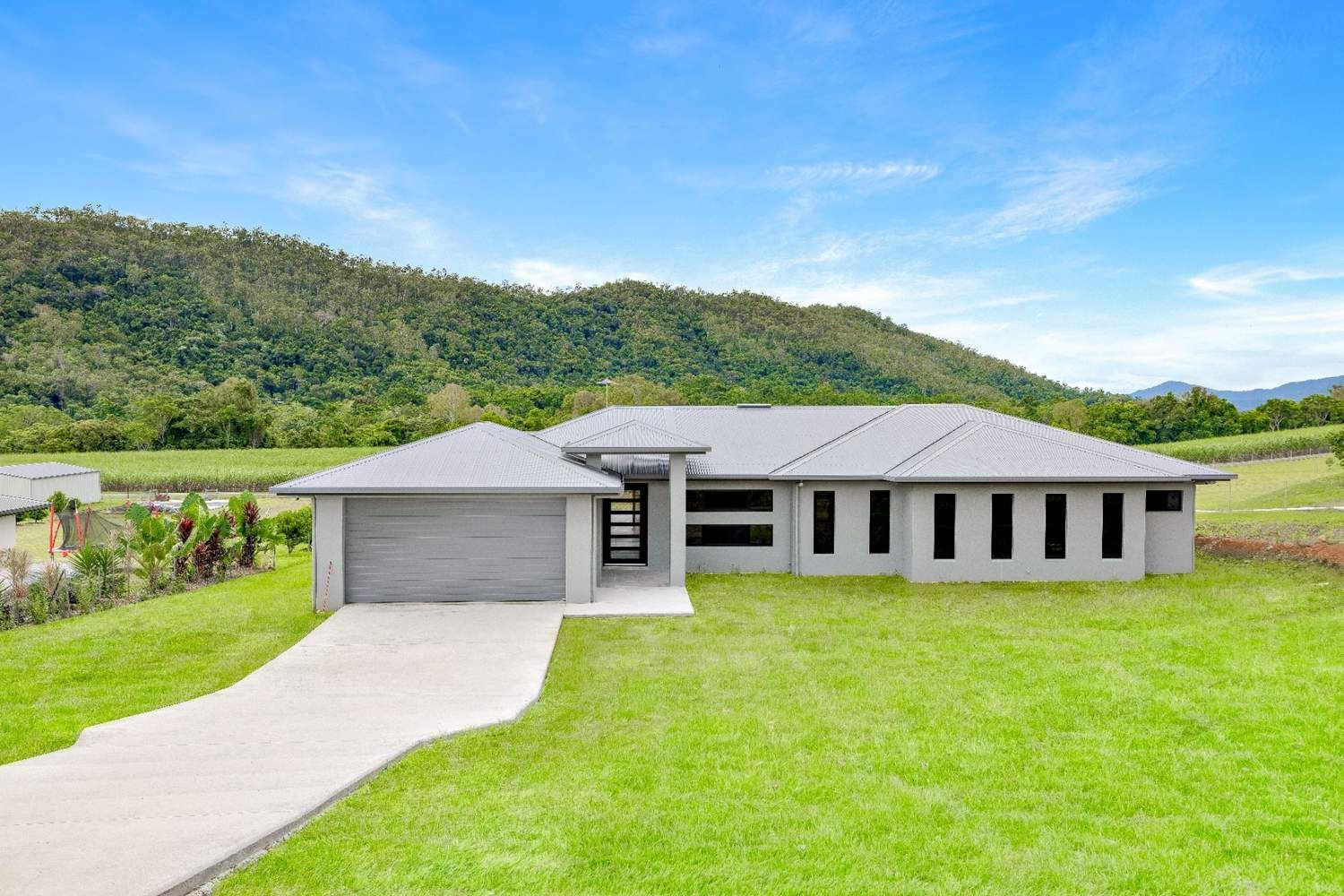 A House is Sitting on Top of a Lush Green Hillside With Mountains in the Background — Ashlee Jones Homes in Gordonvale, QLD
