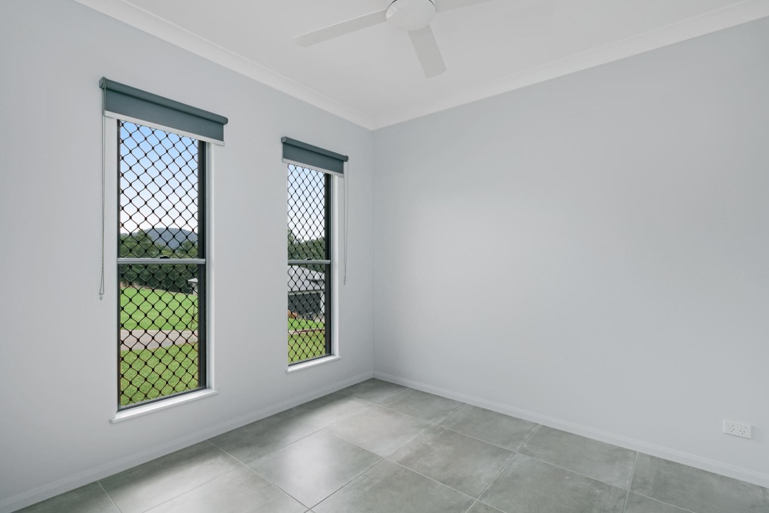 An Empty Room With Two Windows and a Ceiling Fan — Ashlee Jones Homes in Gordonvale, QLD