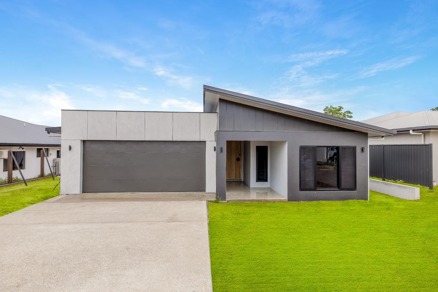 A Modern House with A Large Garage and A Lush Green Lawn in Front of It — Ashlee Jones Homes in Gordonvale, QLD