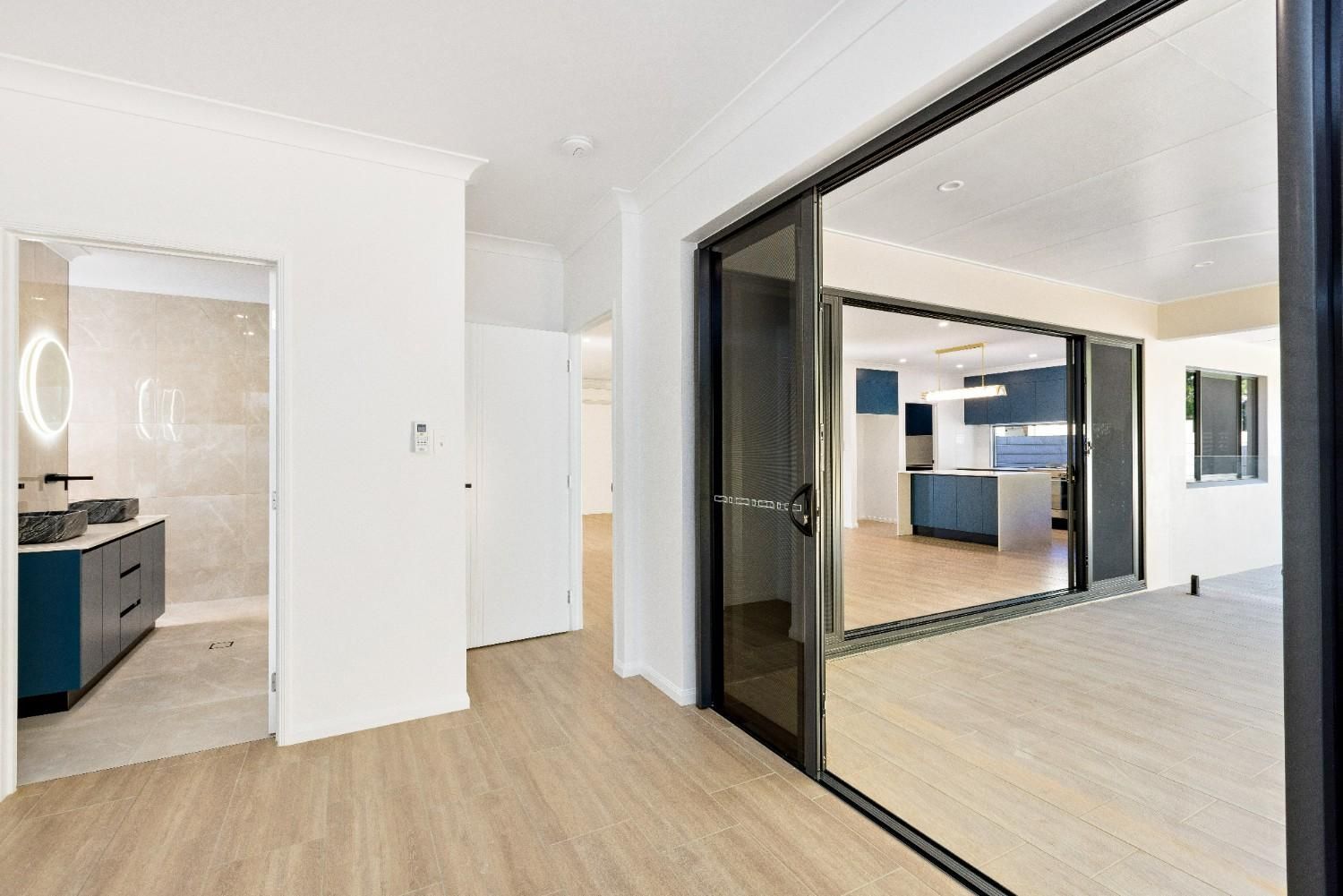 An Empty Room With Sliding Glass Doors Leading to a Bathroom and Kitchen — Ashlee Jones Homes in Gordonvale, QLD