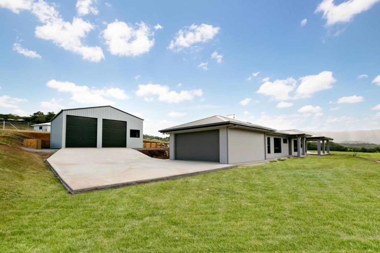 A House With a Garage and a Driveway is Sitting on Top of a Lush Green Field — Ashlee Jones Homes in Gordonvale, QLD