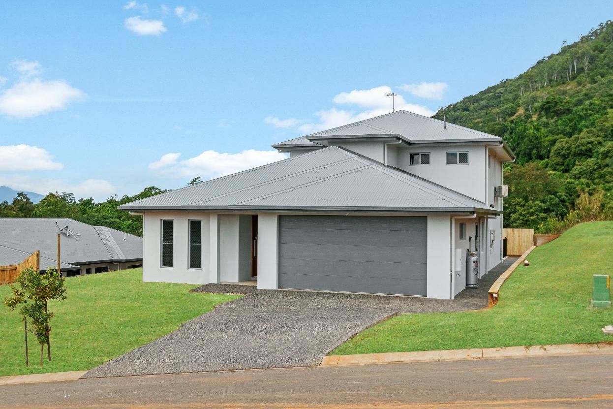 A White House With a Gray Garage Door is Sitting on Top of a Lush Green Hillside — Ashlee Jones Homes in Gordonvale, QLD