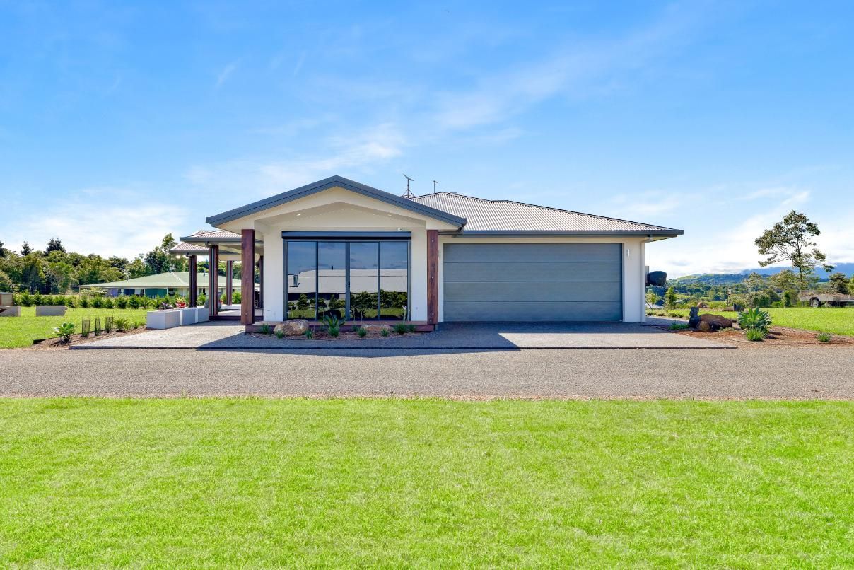 A House With a Garage is Sitting on Top of a Lush Green Field — Ashlee Jones Homes in Gordonvale, QLD