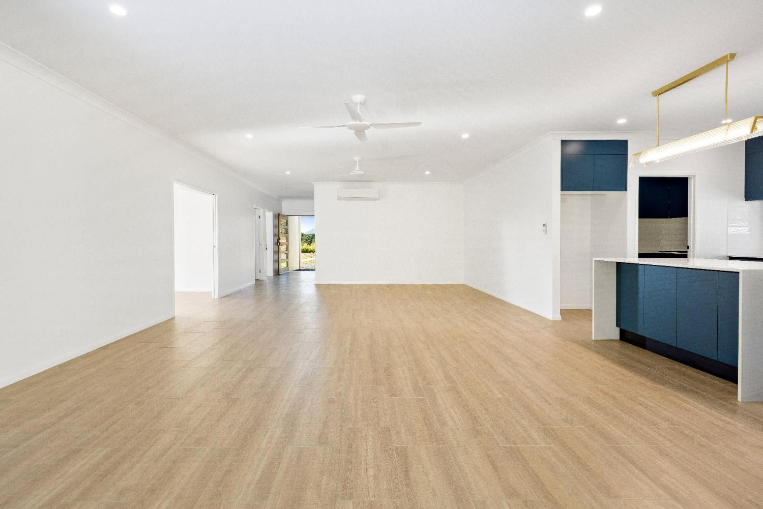 A Large Empty Room With Wooden Floors and White Walls — Ashlee Jones Homes in Gordonvale, QLD