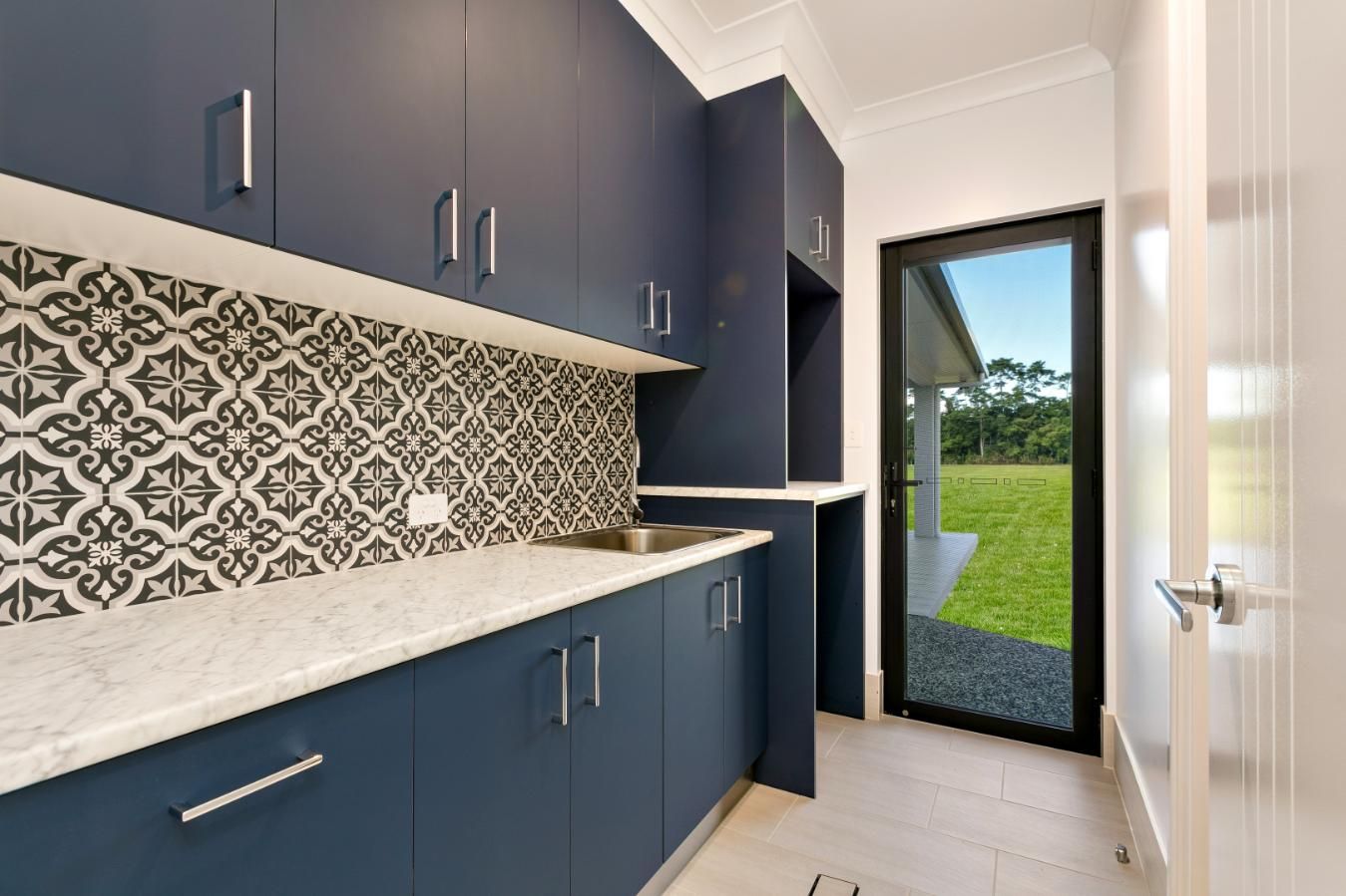 A Kitchen With Blue Cabinets, White Countertops, a Sink and a Sliding Glass Door — Ashlee Jones Homes in Gordonvale, QLD