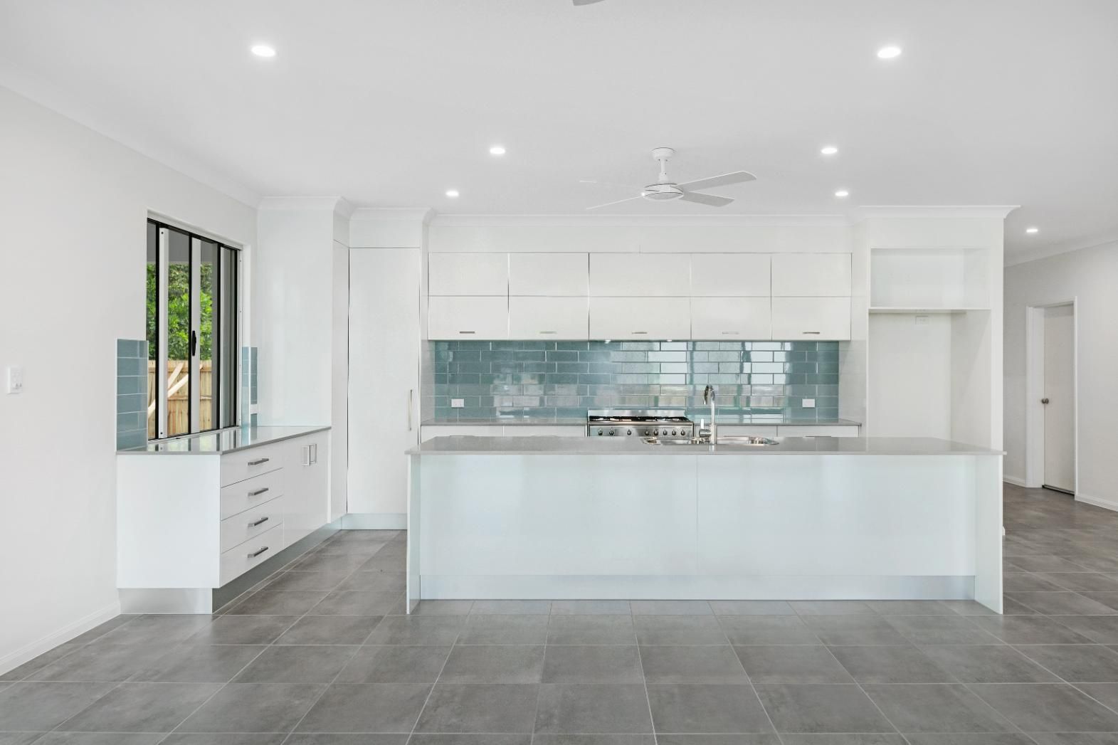 An Empty Kitchen With White Cabinets and a Large Island — Ashlee Jones Homes in Gordonvale, QLD