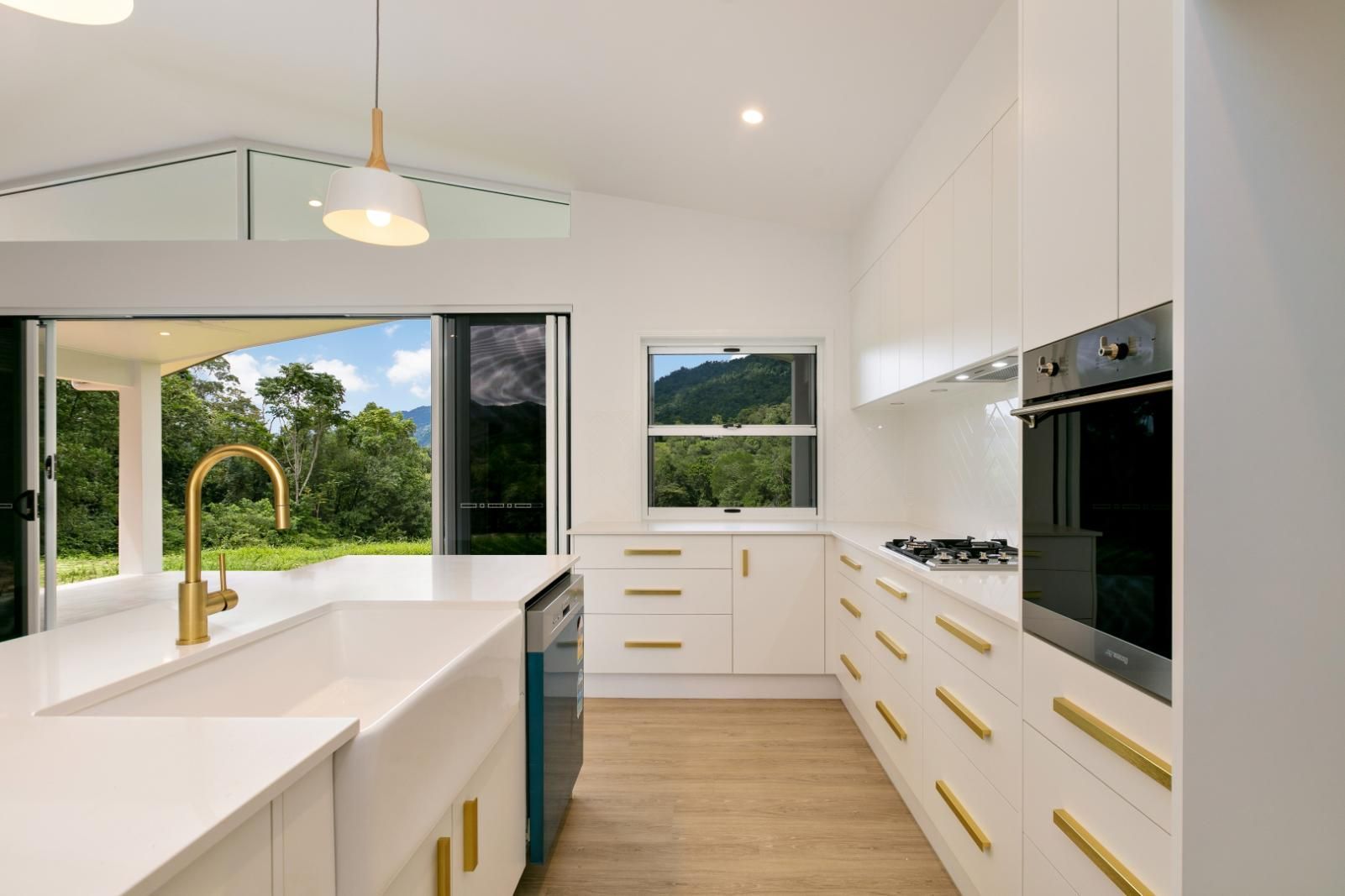 A Kitchen With White Cabinets and Gold Handles and a Large Window — Ashlee Jones Homes in Gordonvale, QLD