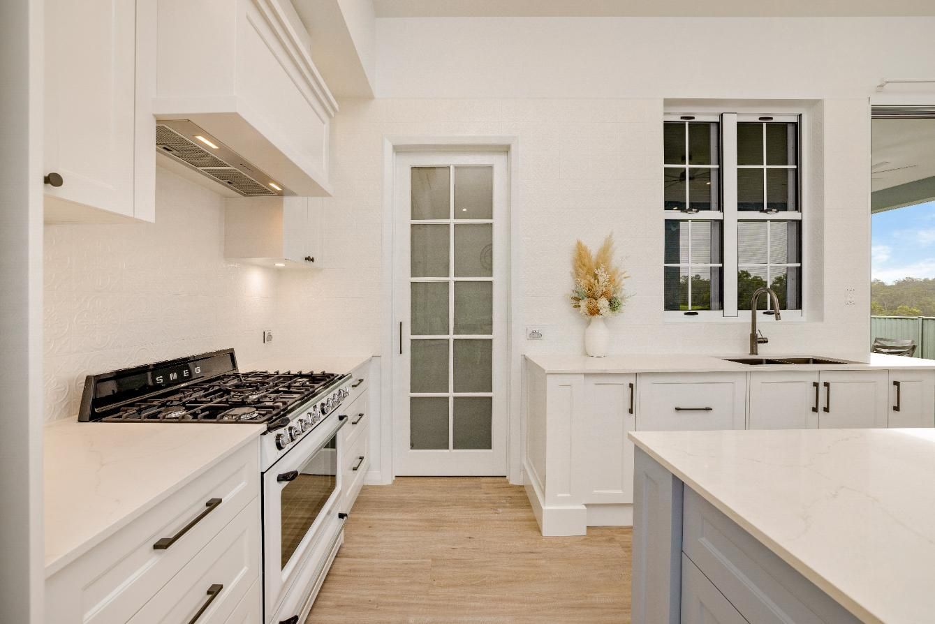 A Kitchen With White Cabinets and a Stove Top Oven — Ashlee Jones Homes in Gordonvale, QLD