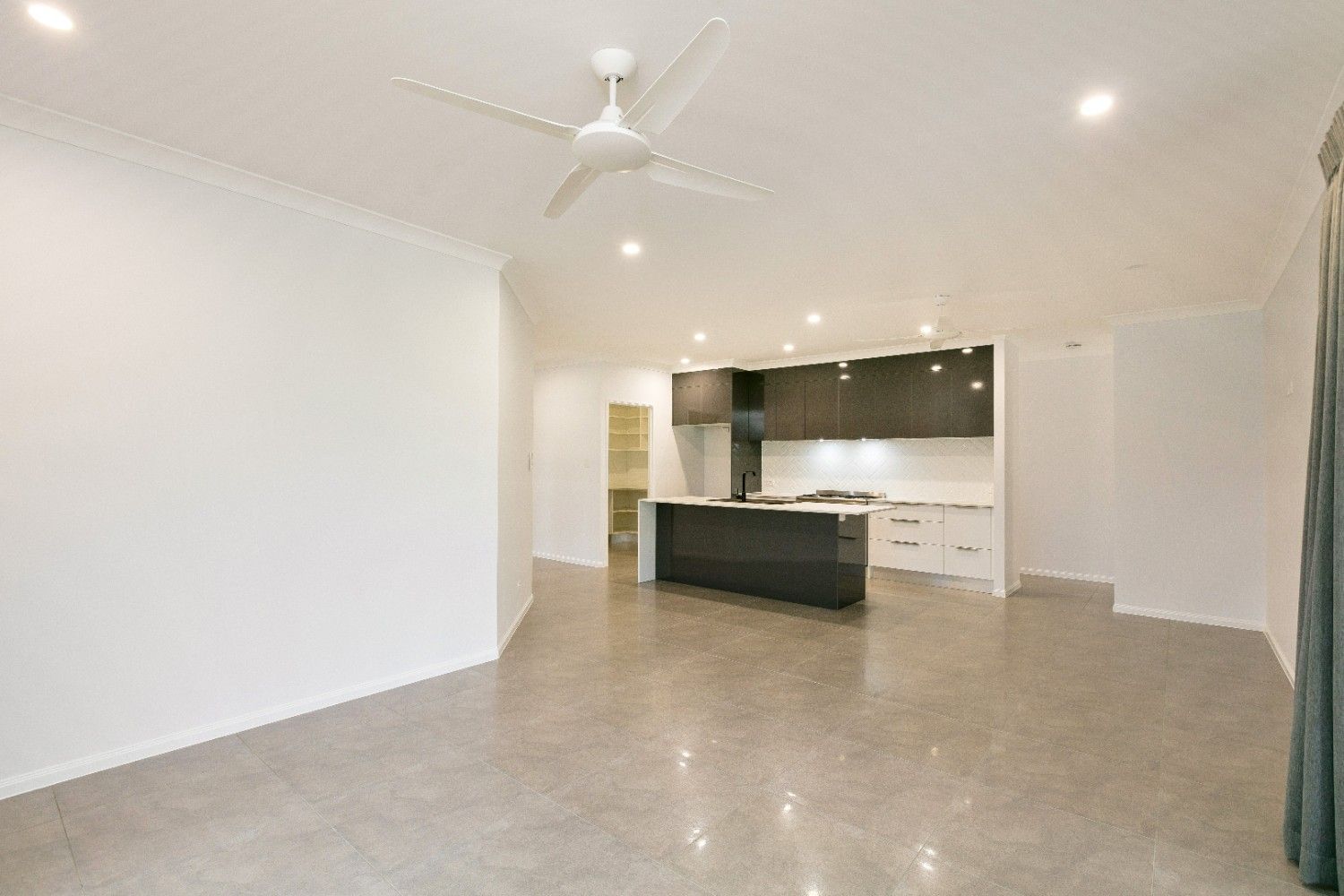 A Living Room With a Ceiling Fan and a Kitchen in the Background — Ashlee Jones Homes in Gordonvale, QLD