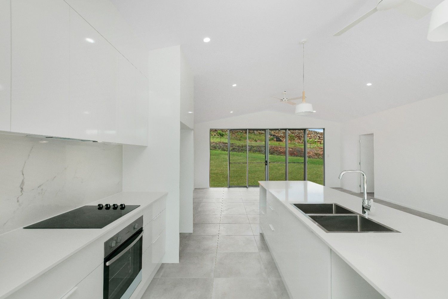 A Kitchen With White Cabinets , a Stove Top Oven, a Sink, and a Large Window — Ashlee Jones Homes in Gordonvale, QLD
