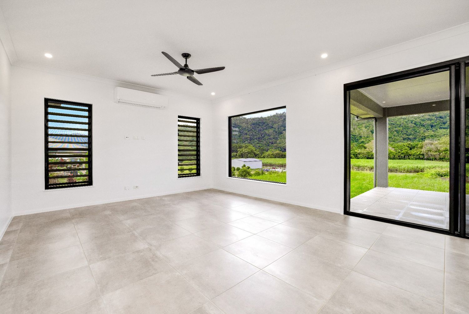 An Empty Living Room With a Ceiling Fan and Sliding Glass Doors — Ashlee Jones Homes in Gordonvale, QLD