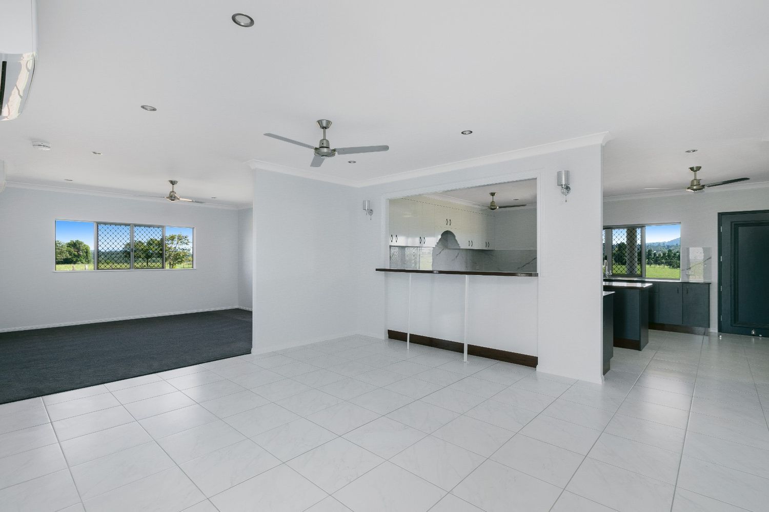A Large Empty Room With a Ceiling Fan and a Kitchen in the Background — Ashlee Jones Homes in Gordonvale, QLD